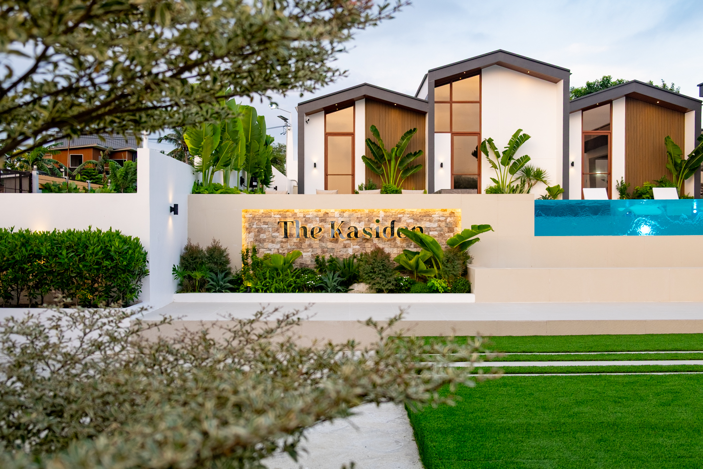 The Kasiden resort signage surrounded by tropical plants and modern villa architecture.