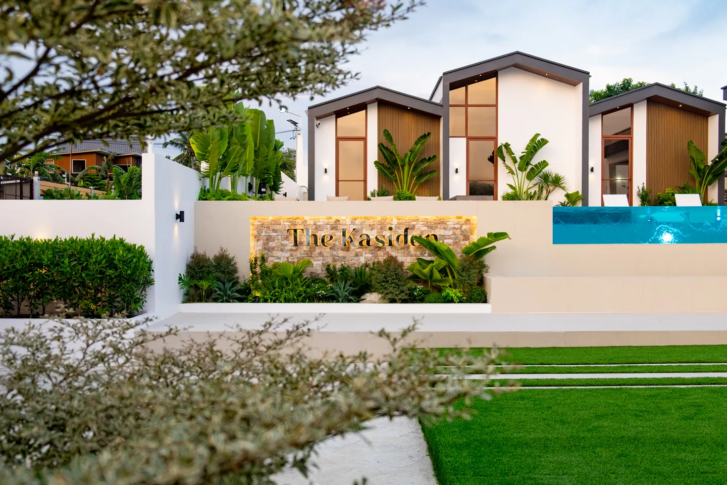 The Kasiden resort signage surrounded by tropical plants and modern villa architecture.