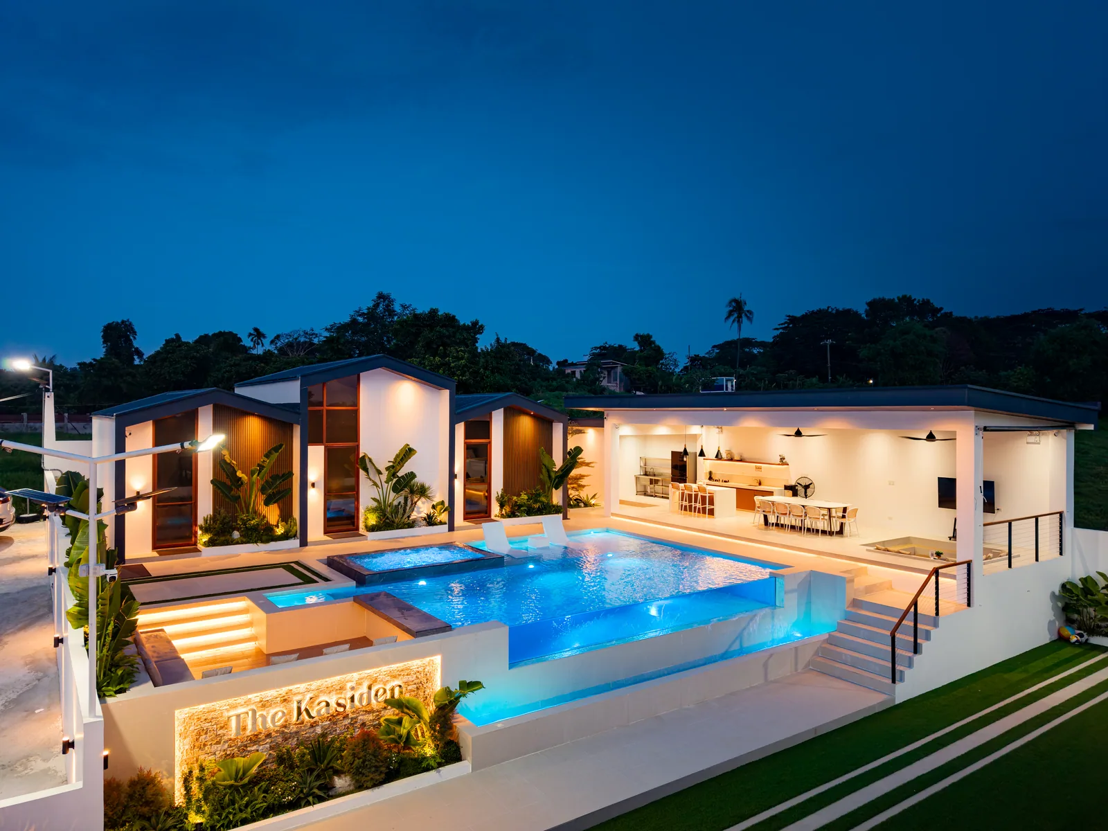 Nighttime aerial view of The Kasiden Private Resort in Alfonso, Cavite featuring modern villas, an illuminated infinity pool with jacuzzi, outdoor dining area, and landscaped surroundings.