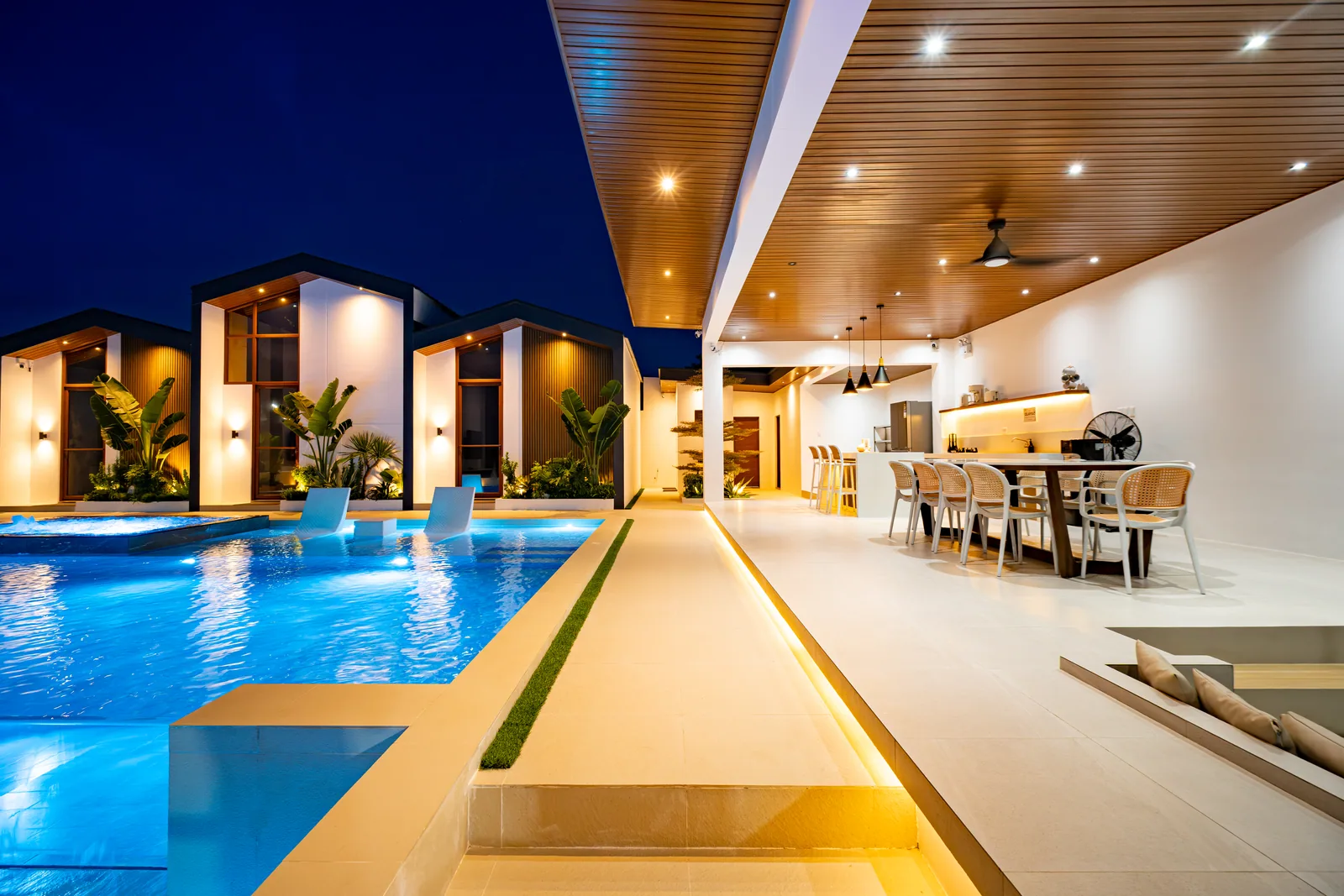 Poolside dining and kitchen area beside the illuminated infinity pool at The Kasiden.